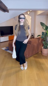 Hallitusest gray t-särk, mustad lühikesed püksid ja valged slip-on jalanõud. Aksessuaaride hulka kuuluvad tumedad päikeseprillid ja väike valge kott. Siseruumides asuv keskkond taimedega.