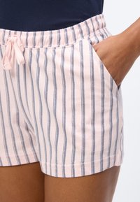 Χέρι στην τσέπη φορώντας ανοιχτό ροζ σορτσάκι με κάθετες ναυτικές ρίγες και ελαστική μέση με κορδόνι, συνδυασμένο με ναυτικό τοπ.