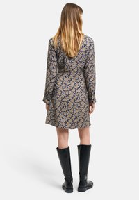 Rochie cu model floral în nuanțe de bleumarin și aur, cu mâneci lungi și croială până la genunchi, completată cu cizme negre până la genunchi.