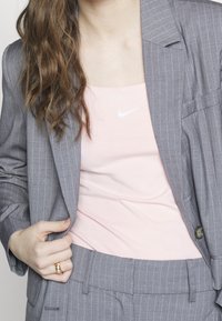 Gray pinstriped blazer over a light pink tank top with a white Nike logo, featuring structured shoulders and a close-fitting silhouette.