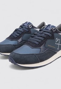 Zapatillas azul marino hechas de malla y ante, con cordones, suela acolchada y un logotipo en el lateral. Diseño duradero con texturas contrastantes.