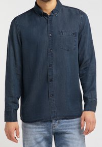 Ciemnoniebieska koszula na guziki z miękkiego materiału, z małą kieszonką na piersi, długimi rękawami i zaokrąglonym dołem.