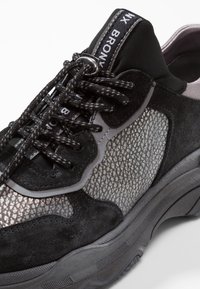 Mustat mokkanahka- ja verkkokankaiset lenkkarit, joissa on teksturoitu harmaa kuvio, tummat nauhat ja pehmustettu pohja; sisältää brändätyt kielen ja kannan.