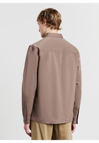 Braune leichte Bluse mit glatter Textur, langen Ärmeln, klassischem Kragen und geknöpften Manschetten, kombiniert mit beigen Hosen.