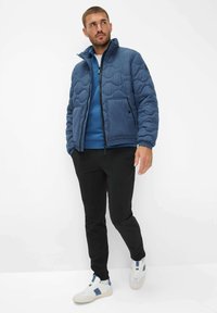 Blå quilted dunjakke med høj krave, parret med en matchende blå sweatshirt og sorte bukser, båret med hvide sneakers.