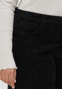 Pantalonii din catifea neagră au nervuri verticale, o buză frontală și un braț. Întregul outfit este completat cu un tricou ușor, cu dungi, cu mânecă lungă.