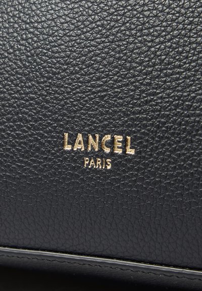 Черен текстуриран кожен материал с златно тиснато лого "LANCEL" и "PARIS". Има фина зърнеста структура, която подчертава детайлите на повърхността.