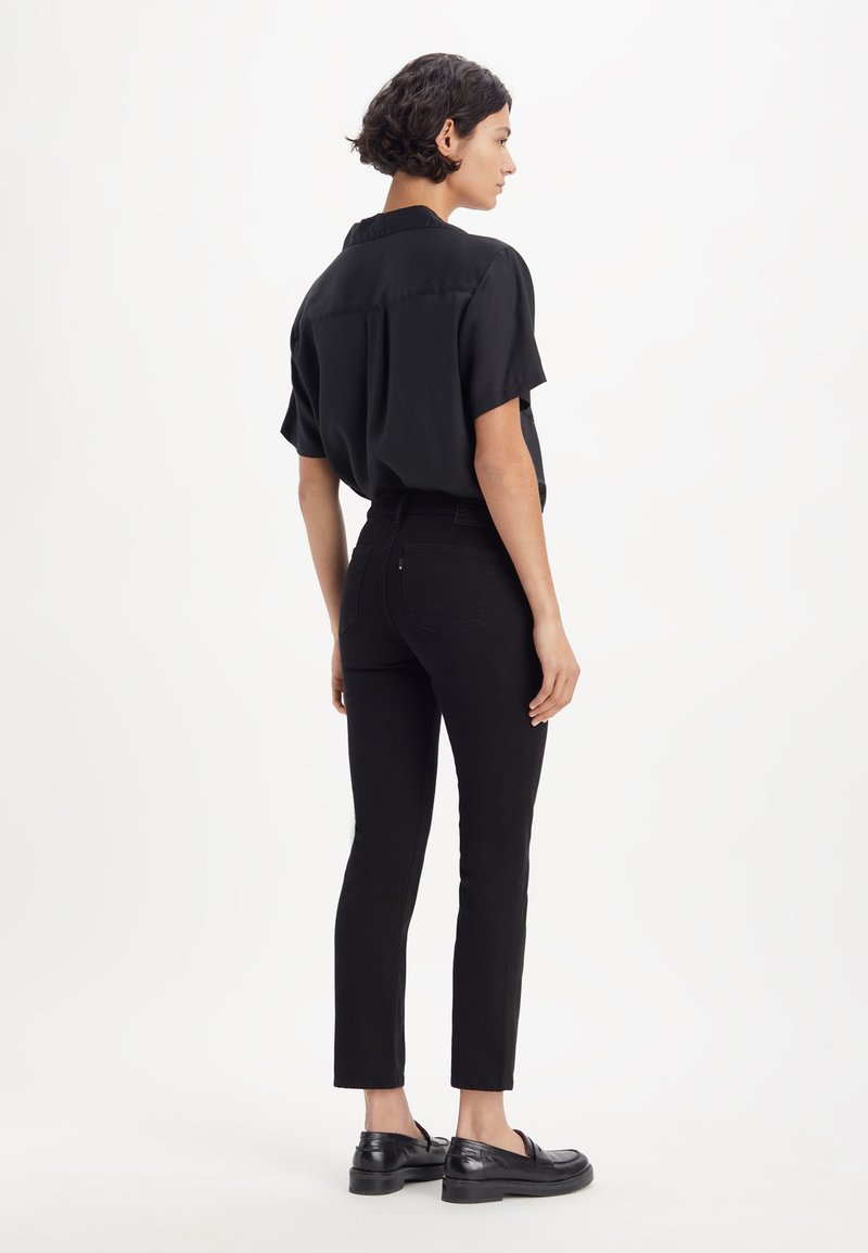 Chemise noire à manches courtes avec des boutons, jean skinny noir et mocassins noirs. Tissu lisse ; design ajusté ; lignes épurées sans motifs ni accents.