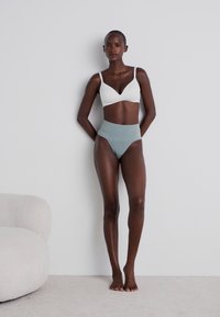 Soutien-gorge léger blanc avec bretelles réglables et culotte taille haute en teal doux, tous deux présentant des textures lisses et un design minimaliste.