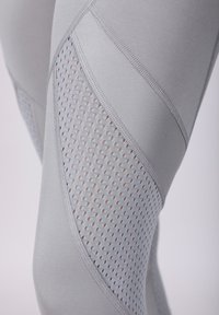 Leggings gris avec un panneau en maille comportant de petites découpes en forme de diamant, texture lisse et coutures renforcées le long des coutures.