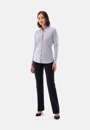 Camicia a maniche lunghe grigia chiara con chiusura a bottoni, con colletto e orlo dritto, abbinata a pantaloni neri su misura e tacchi neri.