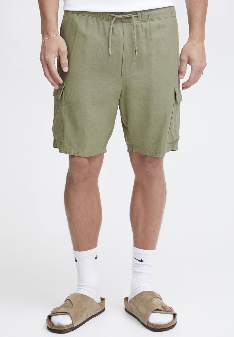 Shorts cargo vert olive avec deux poches latérales, taille élastique et cordon de serrage. Le tissu a une surface texturée et une coupe décontractée.