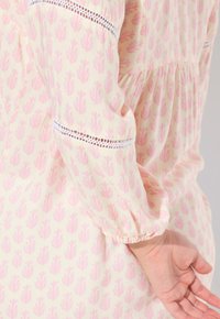Blusa leggera in crema con motivo floreale rosa, maniche elastiche e dettagli in pizzo lungo le maniche. Tessuto testurizzato, vestibilità ampia.