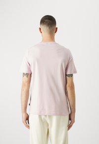 Camiseta de algodón de manga corta y cuello redondo en color rosa claro. Presenta un corte holgado con una textura suave. La vista trasera muestra un mínimo de costuras y detalles.