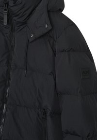 Giacca a vento nera con design trapuntato, colletto alto, chiusura con zip e tasca laterale; include una patch con il marchio sul manica.