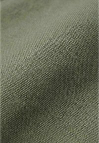 Nærbilde av teksturert olivengrønt stoff med et vevd mønster og en svak fold som skaper myke skygger.