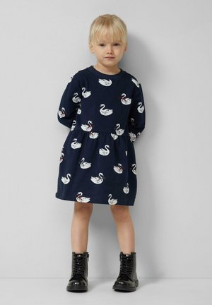 Robe en coton bleu marine avec un motif de cygne, des manches longues, une couture à la taille et une jupe évasée. Associée à des bottes noires à lacets.