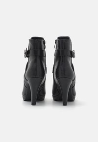 Botines de cuero negro con tacón alto, que cuentan con un cierre de cremallera y detalles decorativos de hebilla. Textura suave y diseño ajustado.