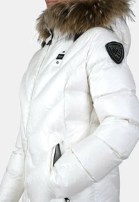 Giacca a vento bianca con cappuccio in pelliccia staccabile, apertura con zip, motivo trapuntato e topper con logo nero sulla spalla sinistra.