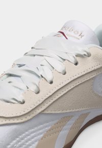 Κοντινό πλάνο λευκού και μπεζ sneaker Reebok με επικάλυψη από σουέτ και λευκά σατέν κορδόνια σε ανοιχτό φόντο.