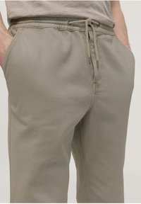 Ljusbeige sweatpants tillverkade av ett mjukt bomullsmaterial, med elastisk midja och snörning, sidfickor och en avslappnad passform.