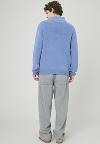 Pull en maille bleu clair avec un col haut, finition texturée, manches longues et poignets côtelés, associé à un jean gris ample.