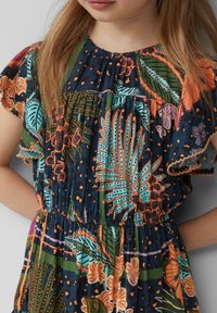 Blumenkleid mit kurzen Rüschensäumen, das einen marineblauen Hintergrund und lebhafte tropische Muster in Orange, Grün und Türkis aufweist.