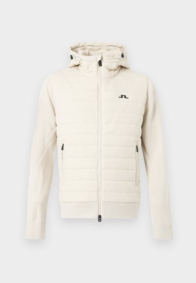 Μπουφάν σε εκρού χρώμα με επένδυση, κουκούλα, πλήρης φερμουάρ μπροστά, πλαϊνές τσέπες με φερμουάρ και μικρό μαύρο λογότυπο στο στήθος.