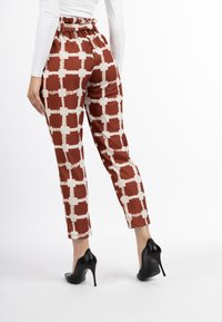 Bruine en crème gemarmerde broek met een ruffel tailleband, taps toelopende pijpen en een gladde, glanzende textuur, gecombineerd met zwarte hoge hakken.