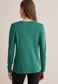 Green long-sleeve sweater made of soft knit material, featuring a crew neck and ribbed cuffs. The design is simple with a relaxed fit.