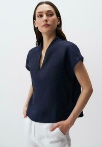Top in lino blu navy con scollo a V, maniche corte, vestibilità rilassata e texture sottile, abbinato a pantaloni chiari.