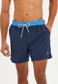 Marineblauwe zwembroek met een elastische tailleband en lichtblauwe trekkoord. Voorzien van zijzakken en een klein logo op de zoom.