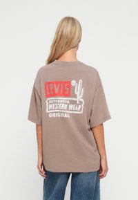 Smeđa prevelika majica s grafičkim printom u bojama na leđima s natpisima "Levi's", "Autentična zapadna odjeća" i ilustracijom kaktusa.