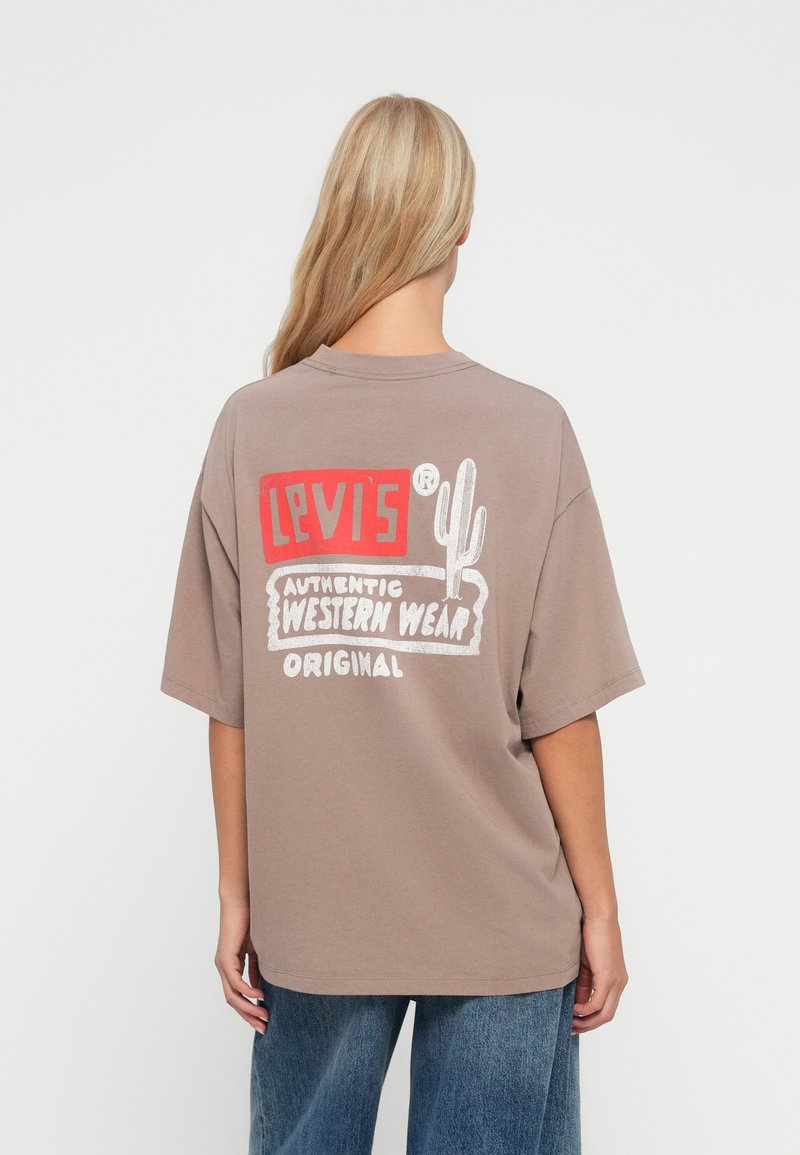 Smeđa prevelika majica s grafičkim printom u bojama na leđima s natpisima "Levi's", "Autentična zapadna odjeća" i ilustracijom kaktusa.