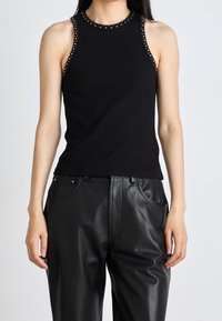 Černý bezrukávový top s žebrovanou strukturou a cvočky podél výstřihu, doplněný o černé kožené kalhoty s vysokým pasem.