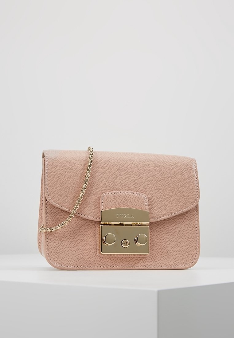 Piccola borsa in pelle saffiano rosa blush con finitura testurizzata, dotata di tracolla in catena dorata e chiusura con gancio dorato, esposta su una superficie bianca contro uno sfondo grigio chiaro.