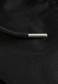 Svart flätad kabel med en metallisk silverändkåpa, på en texturerad svart yta. Fokusera på dess cylindriska form och vävda textur.