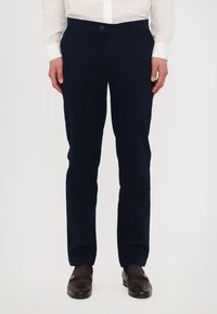 Sötétkék nadrág, szövetből készült, slim fit kialakítással, gombos záródással és oldalsó zsebekkel, barna mokaszinnal párosítva.