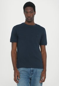 Mørkeblå t-skjorte med korte ermer laget av bomull, med rund hals og en liten logo på venstre bryst, kombinert med lyseblå jeans.