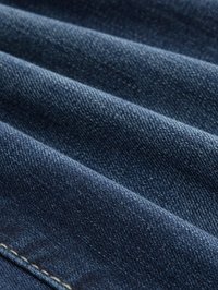Nahaufnahme von gefaltetem dunkelblauem Denimstoff, der Textur und Nahtdetails zeigt.
