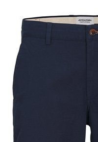 Pantaloni bleumarin cu o țesătură texturată, cu închidere cu buton și bucle pentru curea, etichetați "JACK & JONES" pe banda interioară a taliei.