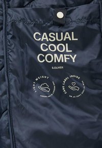 Granatowa tkanina z nadrukowanym białym tekstem: "CASUAL COOL COMFY" oraz ikonami wskazującymi lekkość i instrukcje pielęgnacji. Teksturowana powierzchnia.