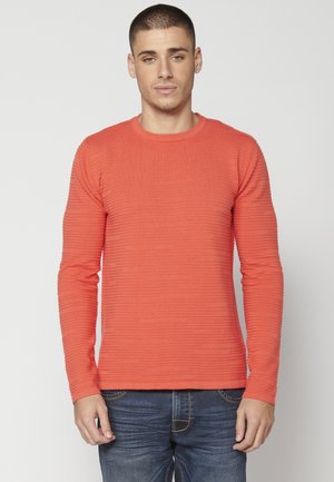 Oranje shirt met lange mouwen en een gestructureerd, ribbelpatroon. Ronde hals, slim fit, gecombineerd met donkerblauwe jeans. Geen zichtbare merknaam.