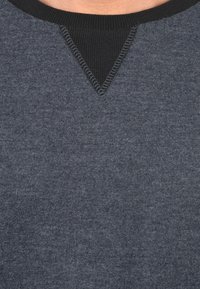 Maglione grigio scuro con un colletto nero a costine e un dettaglio a forma di V sulla parte anteriore. Texture morbida con cuciture a contrasto.