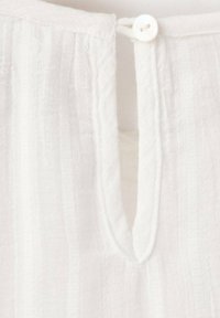 Bílá lněná látka s vertikálním proužkovaným vzorem, s výstřihem do tvaru V a jedním bílým knoflíkem na zadní straně.