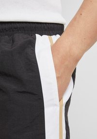 Svart og hvite shorts med teksturert stoff, elastisk midje, sidelomme og en beige detalj langs sømmen.