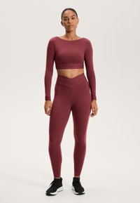 Bordeaux lange mouw crop top in combinatie met high-waisted leggings, voorzien van een opvallende kruisdongelwaardig tailleband, gemaakt van rekbare, zachte stof.