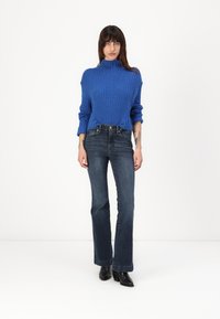 Blå ribbestrikket genser med høy hals, paret med mørk denim flared jeans og svarte ankelstøvler. Enkel og tettsittende design.