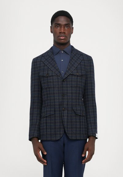 Tengerészkék plaid mintás zakó, amely testhezálló fazonnal rendelkezik, két elülső zseb, gombok és hajtóka gallér található rajta, sötétkék inggel párosítva.