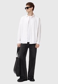 Camisa blanca de botones sobre una camiseta blanca, combinada con vaqueros de pierna ancha oscuros y zapatos negros. Un bolso tote negro complementa el conjunto.